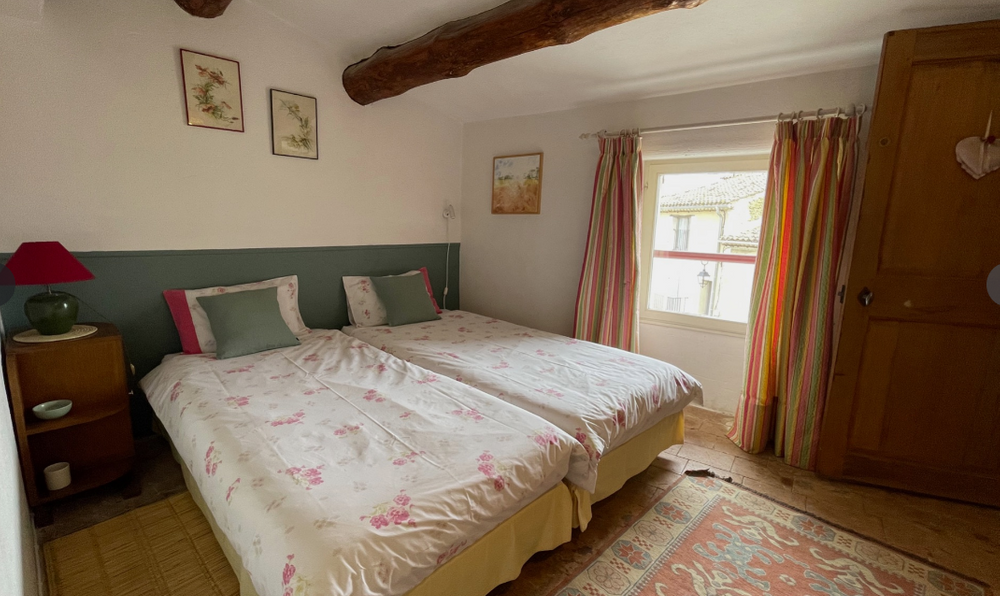 Helles Schlafzimmer von La Cigale in Vaugines mit zwei Einzelbetten, sichtbarem Balken und Blick auf das Dorf
