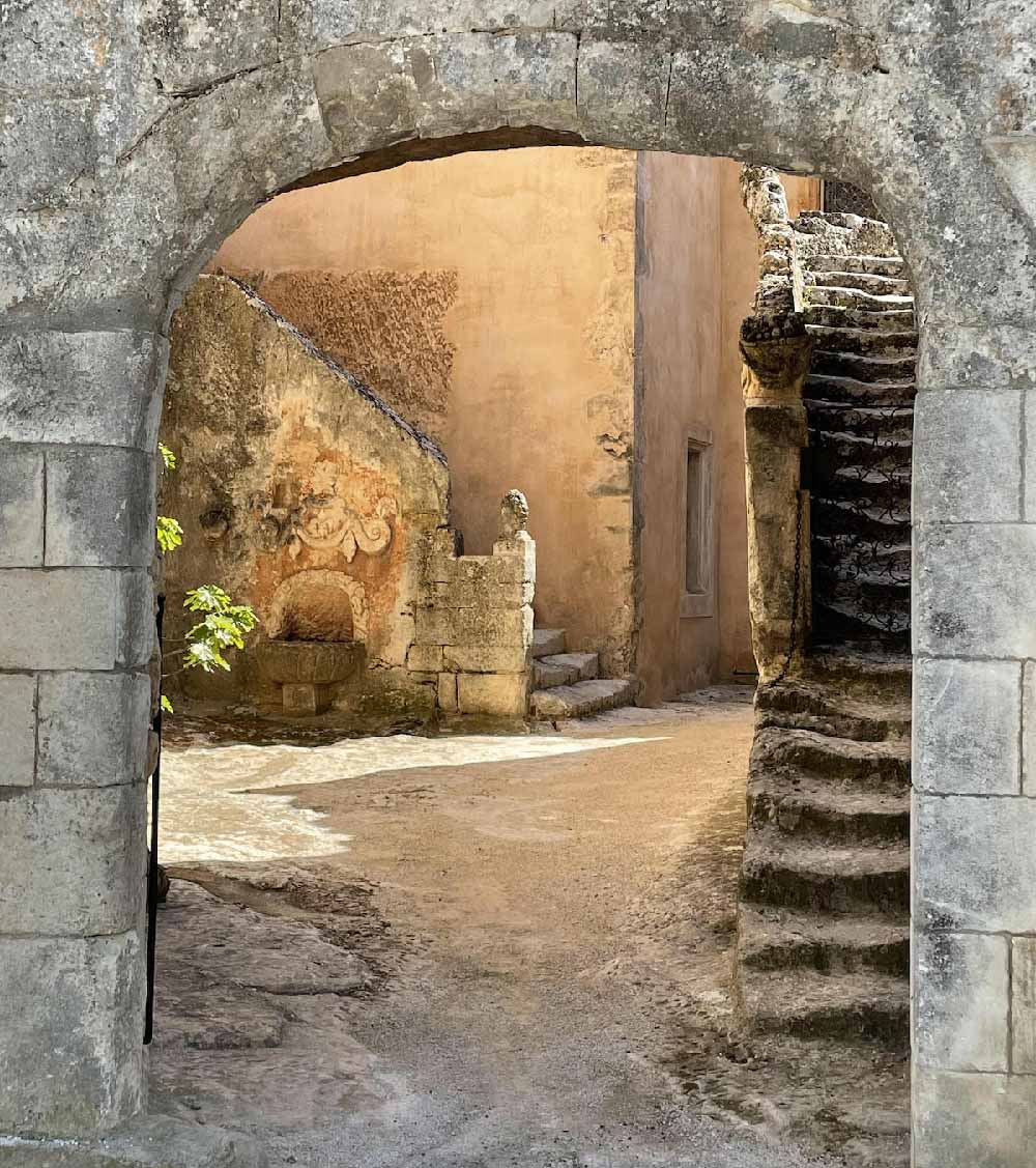 Historischer Torbogen und Innenhof des Château de Mille, ein Ort voller Geschichte. Steinerner Torbogen, der zu einem malerischen Innenhof mit einer antiken Treppe im Château de Mille in Apt führt.