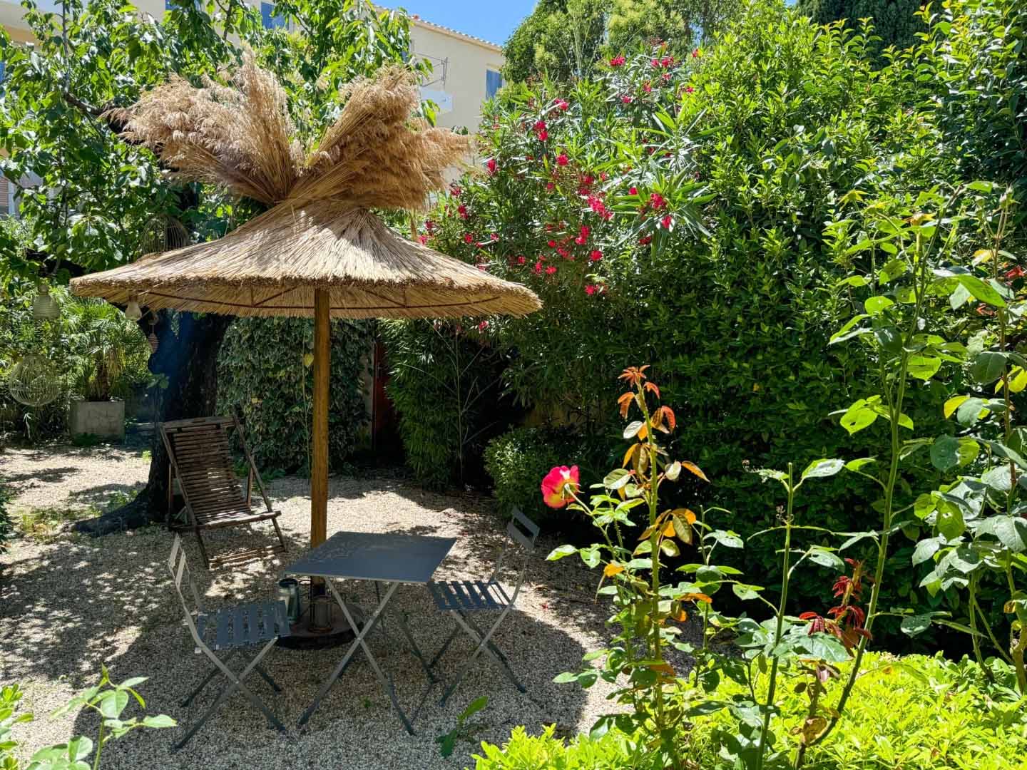 Ein schattiger Entspannungsbereich im üppigen Garten des Nid d'Ange en Provence mit einem Tisch und Stühlen unter einer Bambuspergola.