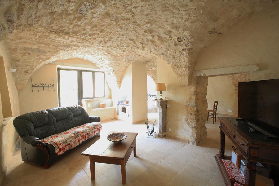 Gewölbtes Wohnzimmer aus Stein in La Petite Maison des Garrigues, mit Sofa und Fernseher