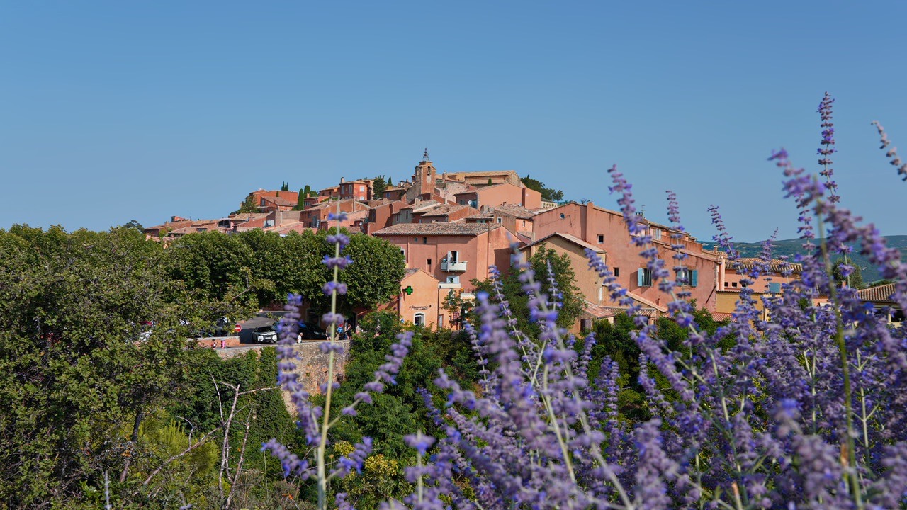 Blick auf das Dorf Roussillon im Luberon mit ockerfarbenen Häusern auf dem Hügel und Lavendel im Vordergrund