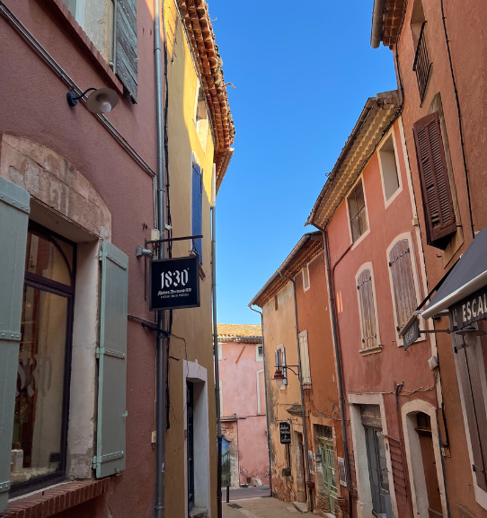 Farbenfrohe Gasse im Dorf Roussillon im Luberon mit ockerfarbenen Fassaden und provenzalischen Häusern