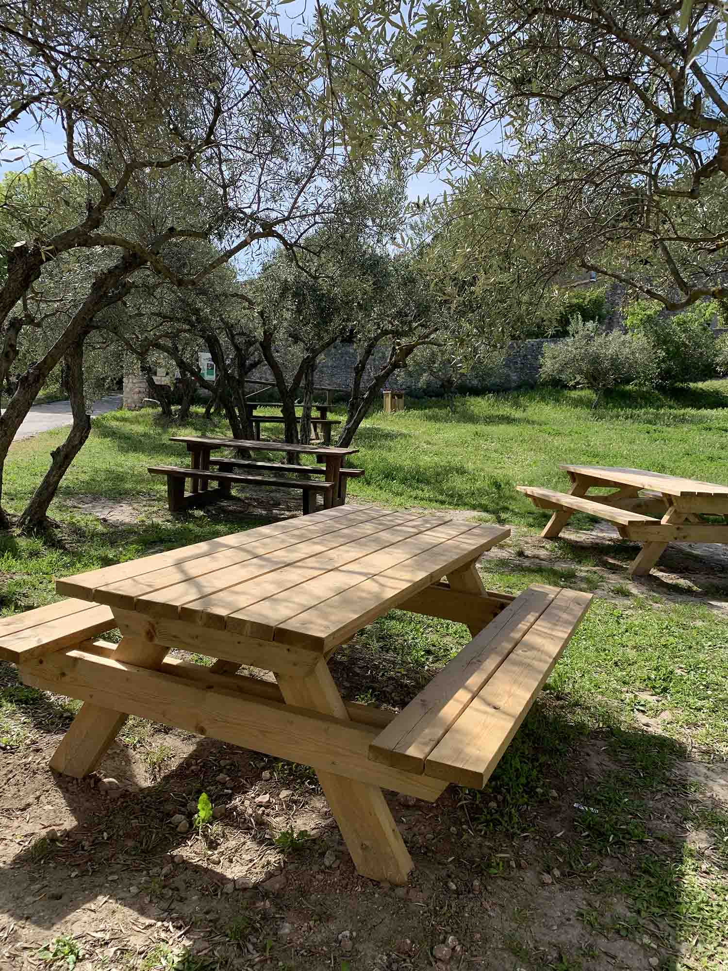 Eine entspannte schattige Pause in der geschützten Umgebung von Mérindol Zwei große doppelte Picknicktische aus Holz auf einer abgegrenzten Kiesfläche, im Schatten von Steineichen im Naturgebiet der Garrigue.