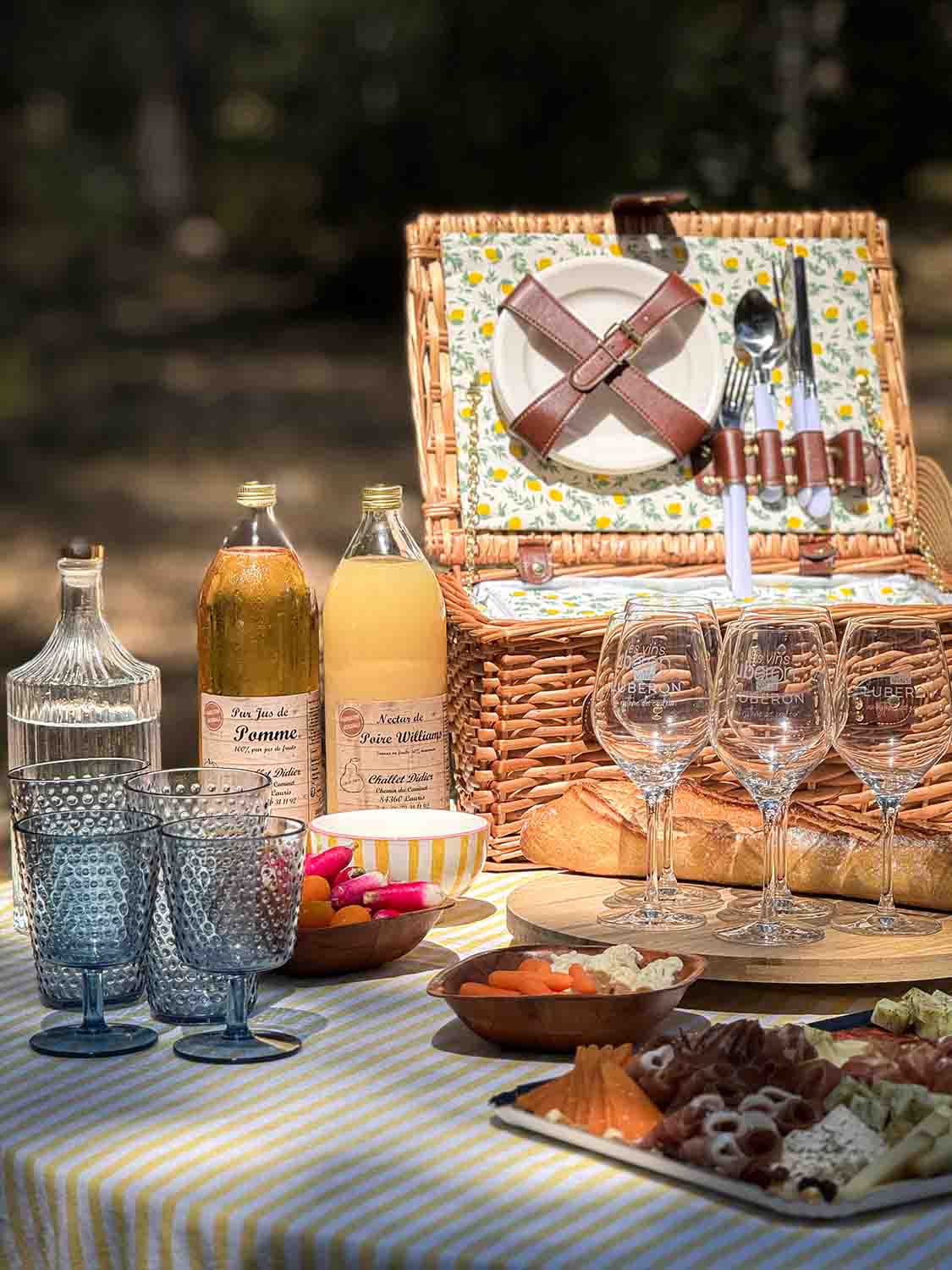 Gefüllter Picknickkorb aus Weidengeflecht mit Gläsern und Flaschen auf einer karierten Decke