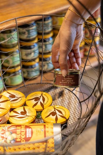 Feinschmeckerprodukte bei Les Délices du Luberon Hand, die ein Feinschmeckerprodukt aus einem Korb bei Les Délices du Luberon nimmt