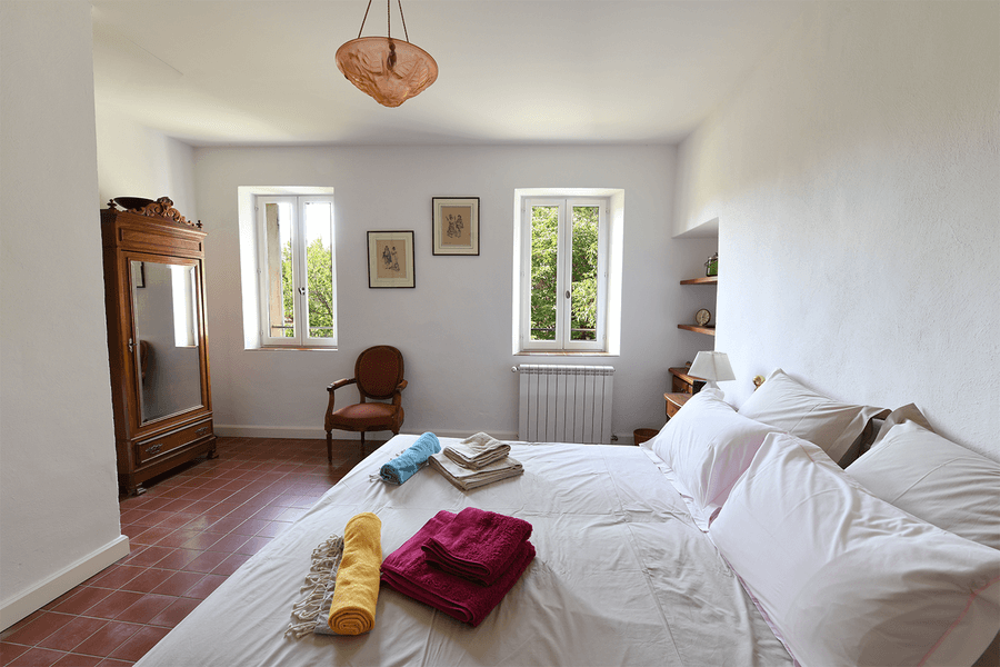 Helles und elegantes Schlafzimmer im Mas du Péressier mit einem Doppelbett, bunten Handtüchern und einem antiken Kleiderschrank.
