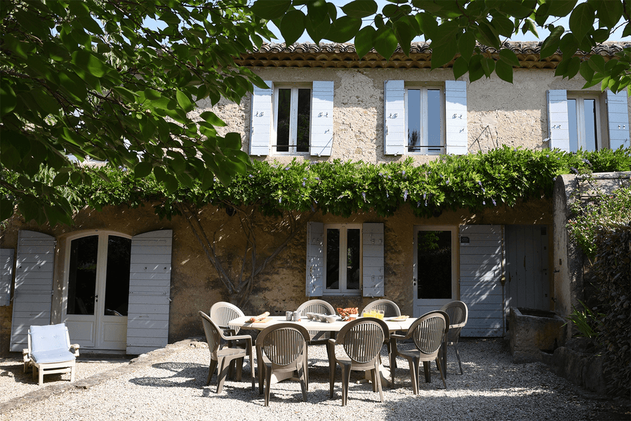 Außenhof des Mas du Péressier mit einem großen Tisch unter einer grünen Pergola in einer typischen Umgebung des Luberon.