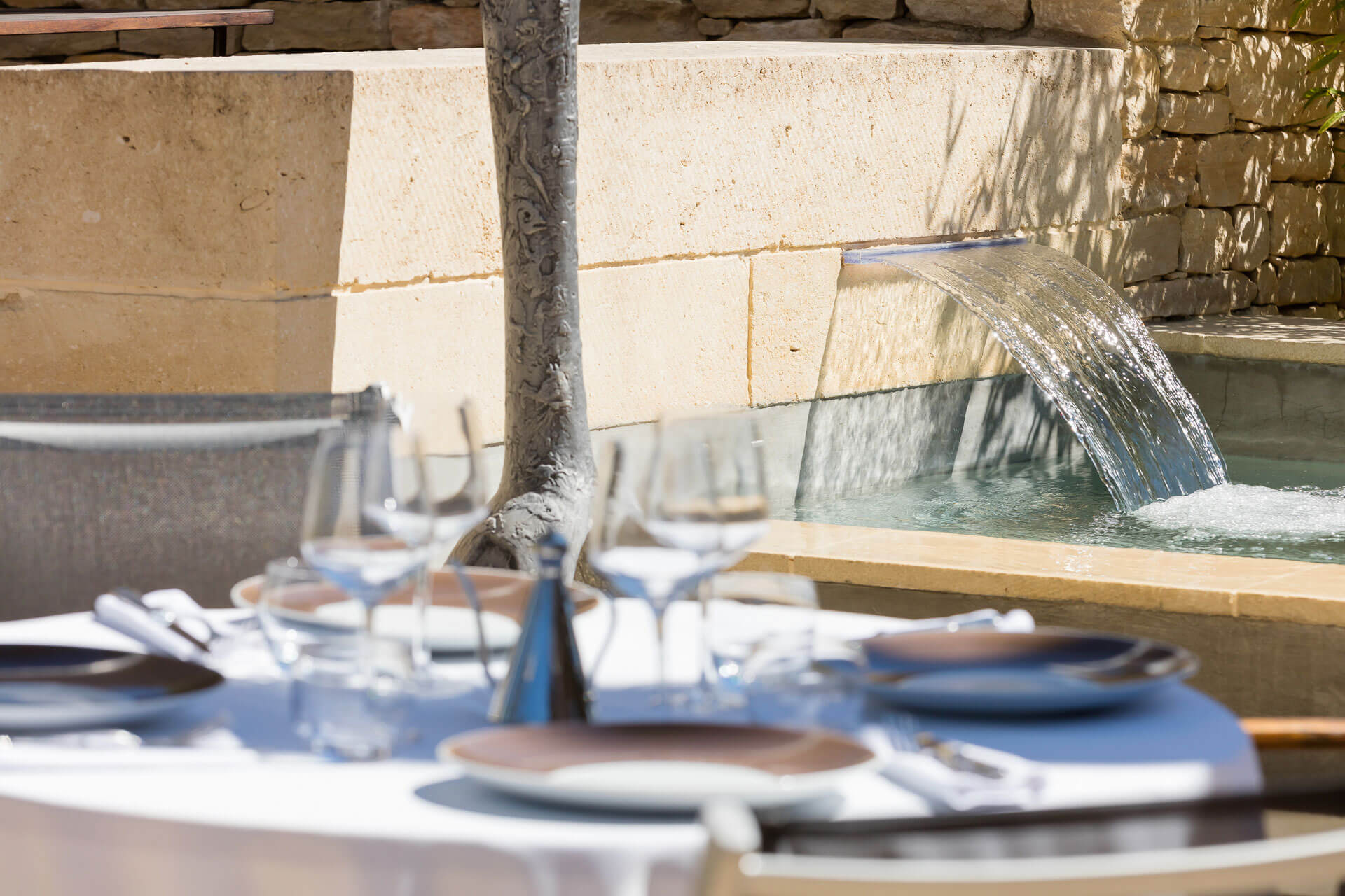 Gedeckter Tisch im Restaurant Le C im Hotel Carcarille in Gordes, nahe einem Wasserbecken mit Brunnen