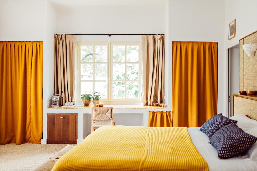 Zimmer im Le Moulin, 4-Sterne-Hotel in Lourmarin, mit Doppelbett, gelber Bettwäsche und ockerfarbenen Vorhängen